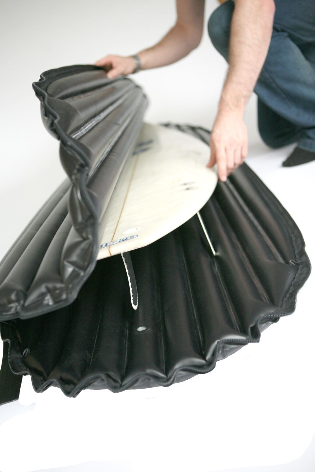 A surfboard being fitted into the open, pleated inflatable cover
